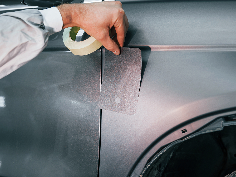 a man comparing a paint color card to a car’s paint finish